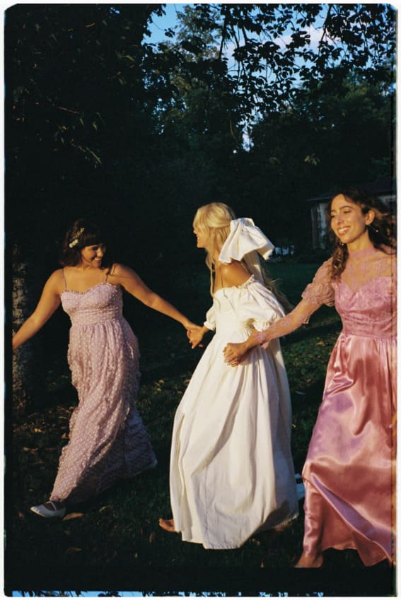 bride with bridesmaids in pink bridesmaids dresses and a white corset wedding dress holding hands
