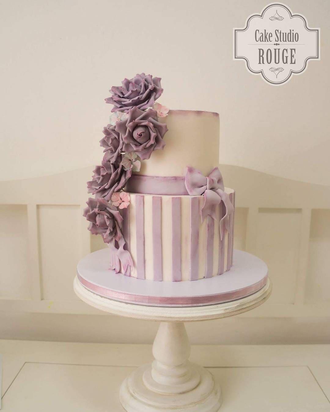 Two-tiered ivory and lavender wedding cake with striped fondant and cascading purple roses