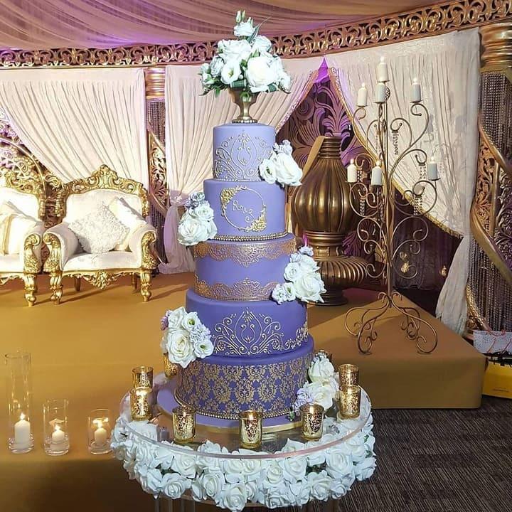 Five-tiered purple wedding cake with gold scrollwork and white roses