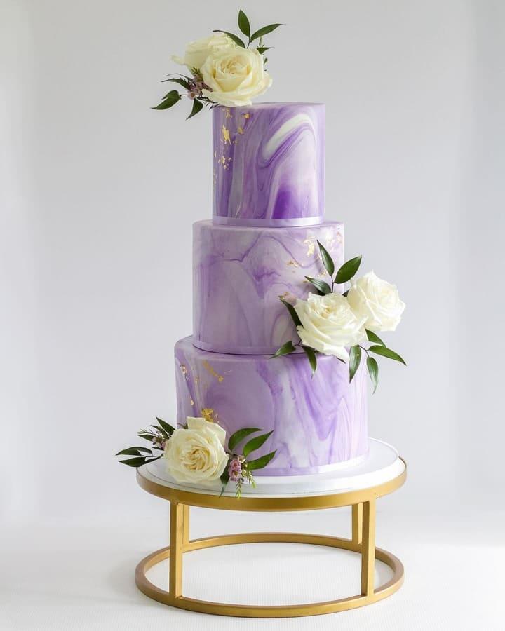 Three-tiered lilac marble wedding cake with gold leaf and ivory roses