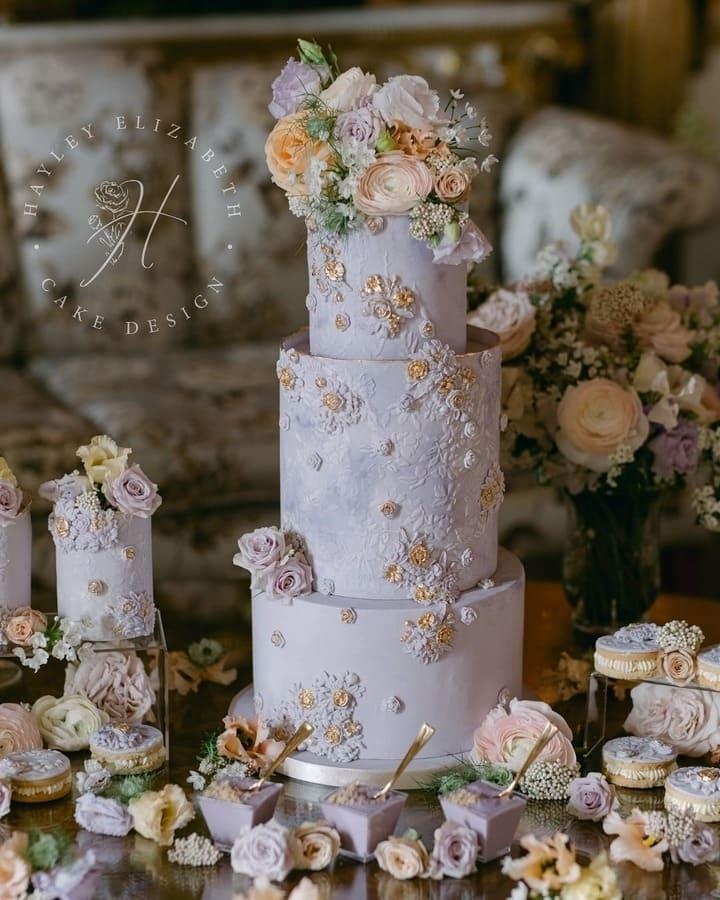 Three-tiered lilac wedding cake with embossed floral texture and pastel flower topper
