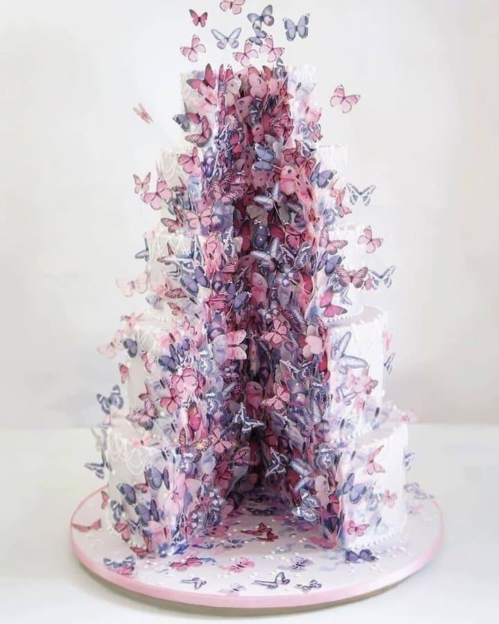 Six-tiered white wedding cake with cascading purple and pink butterflies