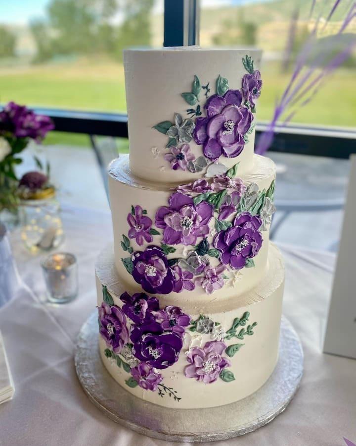 Three-tiered ivory buttercream wedding cake with hand-painted purple florals